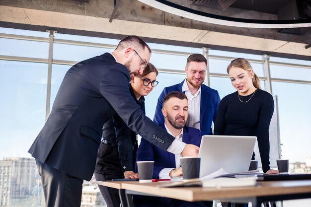 Des gens d'affaires heureux regardant la présentation d'un ordinateur portable, le succès au travail, assis dans un bureau moderne. Négociations en ligne réussies. Les hommes d'affaires partagent leurs connaissances