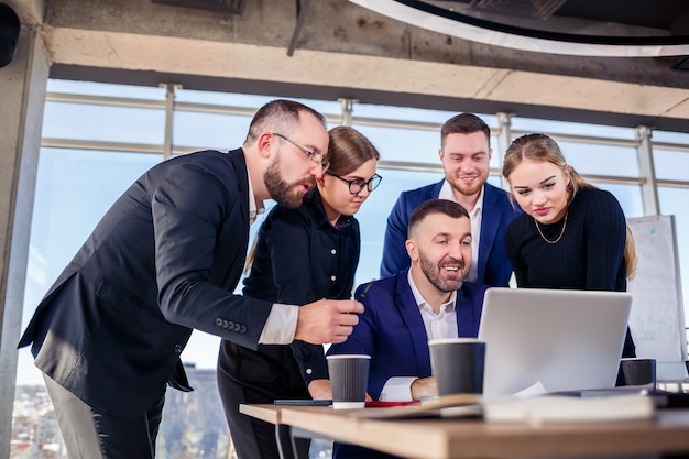 Des gens d'affaires heureux regardant la présentation d'un ordinateur portable, le succès au travail, assis dans un bureau moderne. Négociations en ligne réussies. Les hommes d'affaires partagent leurs connaissances