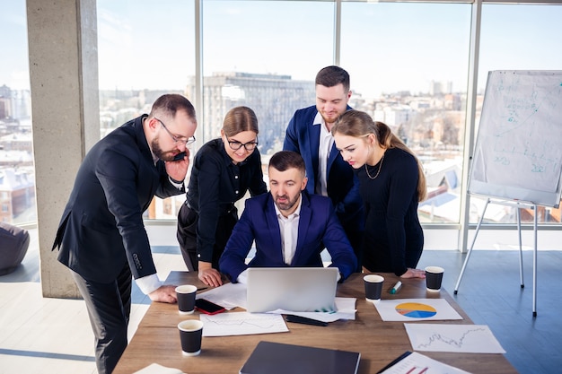 Des gens d'affaires heureux regardant la présentation d'un ordinateur portable, le succès au travail, assis dans un bureau moderne. Négociations en ligne réussies. Les hommes d'affaires partagent leurs connaissances