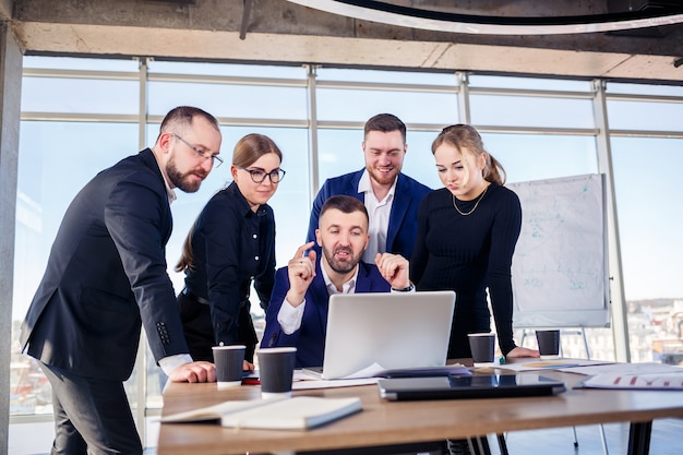 Des gens d'affaires heureux regardant la présentation d'un ordinateur portable, le succès au travail, assis dans un bureau moderne. Négociations en ligne réussies. Les hommes d'affaires partagent leurs connaissances