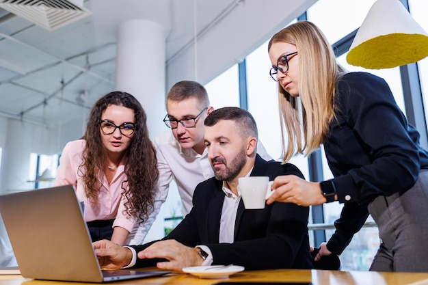 Gens d'affaires heureux regardant la présentation d'un ordinateur portable, succès au travail, assis dans un bureau moderne. Négociations en ligne réussies. Les hommes d'affaires partagent leurs connaissances