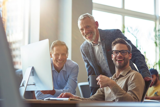 Gens d'affaires heureux trois hommes gais regardant la caméra et souriant tout en étant assis au bureau et