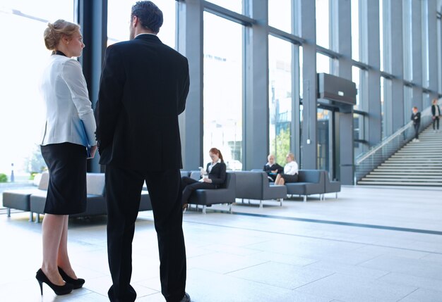 Gens d'affaires modernes discutant pendant la pause debout dans le hall en verre de l'immeuble de bureaux