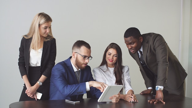 Les gens d'affaires s'assoient et ont une réunion informelle pour examiner ensemble les données sur une tablette numérique.