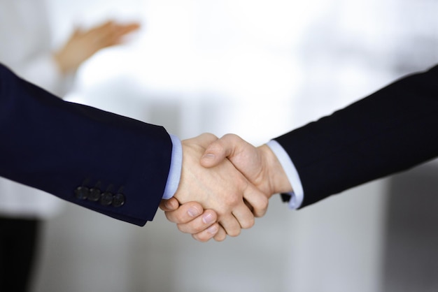 Gens d'affaires se serrant la main lors d'une réunion ou d'une négociation, gros plan. Groupe d'hommes d'affaires inconnus et une femme debout dans un bureau moderne. Concept de travail d'équipe, de partenariat et de poignée de main.