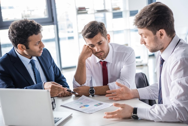 Des gens d'affaires sérieux assis à table et discutant de diagrammes au bureau, concept d'entreprise