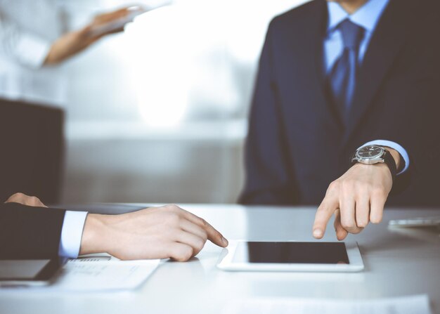 Les gens d'affaires utilisent un ordinateur tablette, tout en travaillant ensemble au bureau dans un bureau moderne. Homme d'affaires inconnu ou entrepreneur masculin assis au bureau avec un collègue et une secrétaire sur le backgro