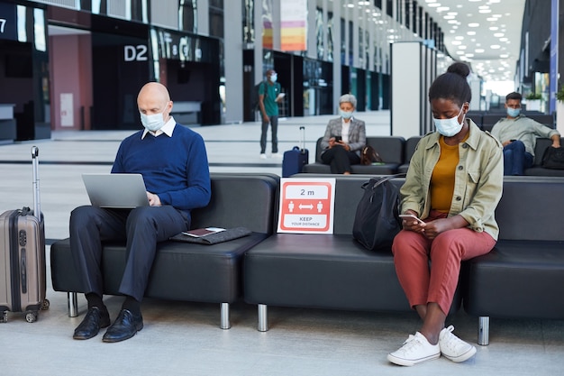 Des gens assis dans la salle d'attente et utilisant des gadgets à l'aéroport