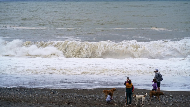 Les gens et les chiens regardent une forte tempête en mer Côte de la mer Noire Orage Orage Orage Les vagues de haute mer pulvérisent de la mousse s'élèvent au-dessus de l'horizon