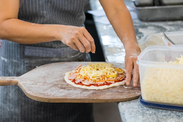 Photo les gens et le concept de cuisine font cuire la main en ajoutant du fromage râpé à la pizza à la pizzeria