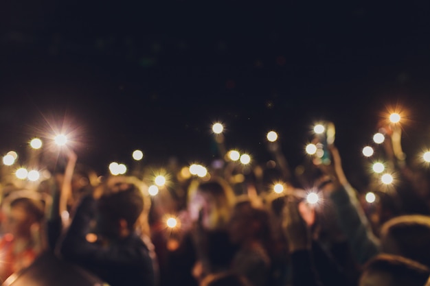 Les gens debout, les bras levés, tournent une vidéo sur le téléphone à un spectacle de musique de rue, arrière-plan flou.