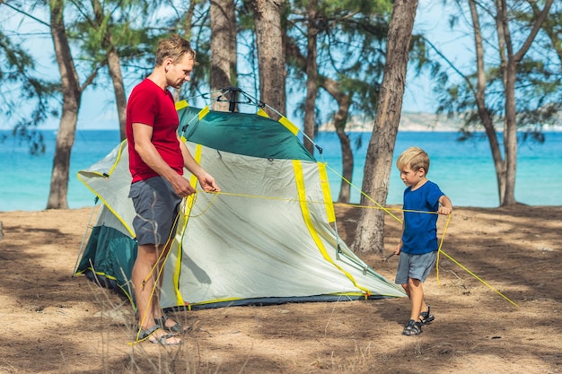 Les gens du camping les touristes de style de vie en plein air ont mis en place un camping gris vert forêt d'été près de la mer de lazur Un garçon aide son père à étudier le mécanisme de la tente moderne facile à plier L'éducation naturelle des enfants