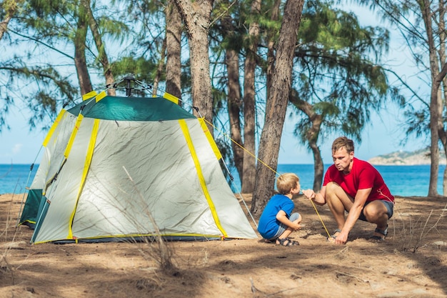 Les gens du camping les touristes de style de vie en plein air ont mis en place un camping gris vert forêt d'été près de la mer de lazur Un garçon aide son père à étudier le mécanisme de la tente moderne facile à plier L'éducation naturelle des enfants