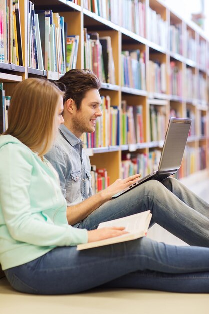 les gens, l'éducation, la technologie et le concept d'école - des étudiants heureux avec un réseau d'ordinateurs portables dans la bibliothèque