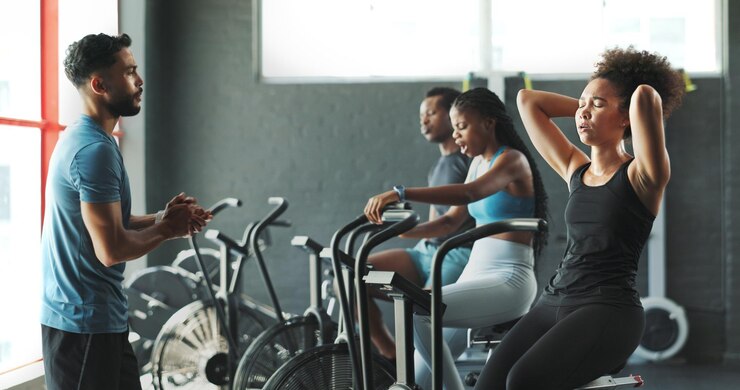 Photo les gens entraîneurs de fitness et fatigué sur le vélo stationnaire à la salle de sport pour l'entraînement d'exercice et l'exercice avec la sueur cyclisme de la machine d'énergie et de la construction des muscles avec le cardio pour la santé, les soins personnels et le bien-être