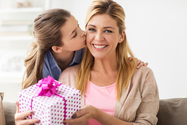 les gens, les fêtes et le concept de la famille - une fille heureuse donnant un cadeau d'anniversaire à sa mère à la maison