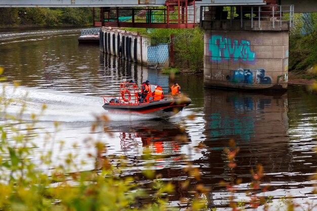 Les gens en gilets de sauvetage sur bateau à moteur flottant sur la rivière sous un pont de fer