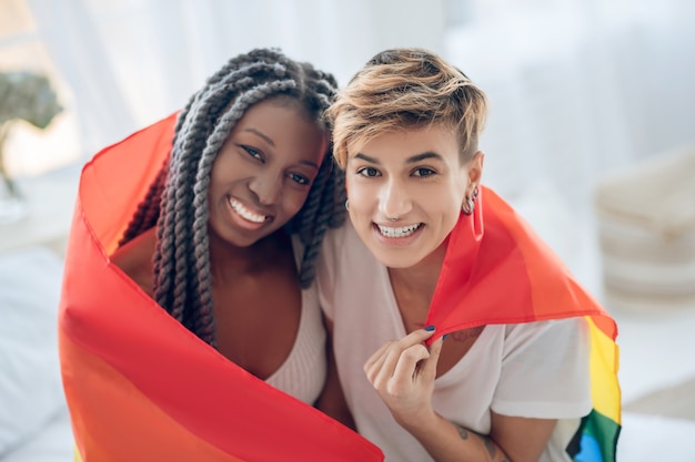 Photo gens heureux. deux jeunes filles avec un drapeau arc-en-ciel souriant positivement