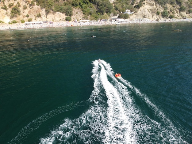 Des gens heureux nagent sur un matelas pneumatique derrière un vélo aquatique à grande vitesse, les touristes montent sur un bateau gonflable