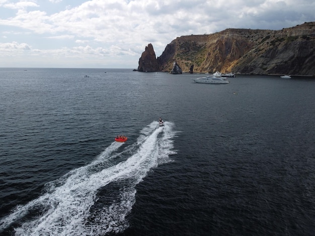 Des gens heureux nagent sur un matelas pneumatique derrière un vélo aquatique à grande vitesse, les touristes montent sur un bateau gonflable