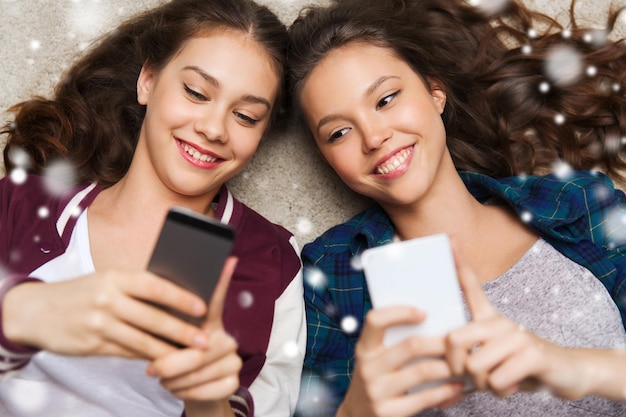 les gens, l'hiver, Noël, la technologie et le concept d'amitié - joyeux souriant jolies adolescentes ou amis allongés sur le sol avec des smartphones sur la neige