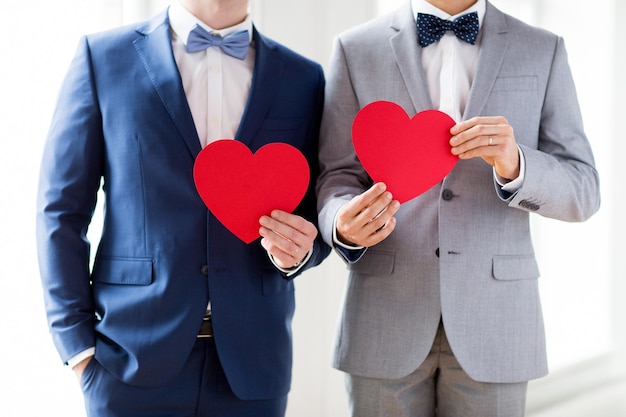 les gens, l'homosexualité, le mariage homosexuel, la saint-valentin et le concept d'amour - gros plan d'un couple gay marié heureux tenant des formes de coeur en papier rouge sur le mariage