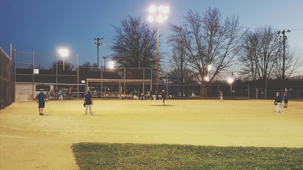 Photo des gens jouant au baseball sur le terrain au crépuscule.