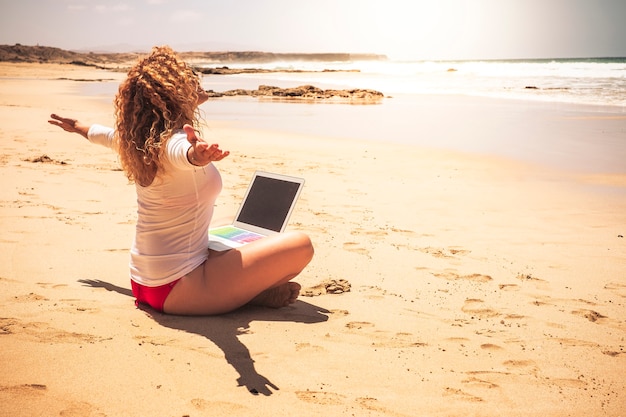 Des gens libres heureux une femme caucasienne s'assoient à l'ebach avec un ordinateur portable sur ses jambes ouvrant les bras profitant de la liberté pour les vacances d'été et pour le travail sans stress bureau dans la ville