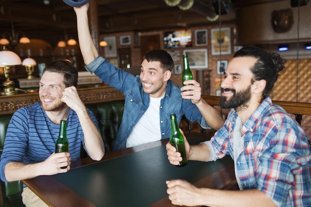 les gens, les loisirs, l'amitié et le concept d'enterrement de vie de garçon - des amis masculins heureux buvant de la bière en bouteille et des mains levées pour un match de football au bar ou au pub