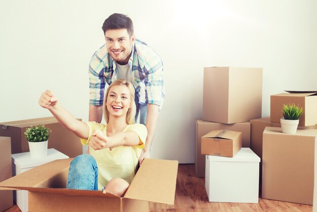 Les gens de la maison déménagent et le concept immobilier couple heureux s'amusant et roulant dans des boîtes en carton à la nouvelle maison