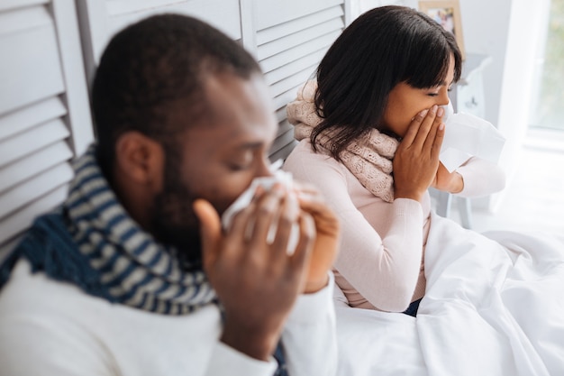 Les gens malades. Beau jeune couple de malades assis à la maison et guérissant leur nez qui coule