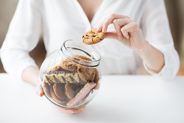 les gens, la malbouffe, la cuisine, la cuisson et le concept de mauvaise alimentation - gros plan des mains avec des biscuits à l'avoine au chocolat et des barres de muesli dans un bocal en verre