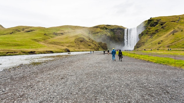 Les gens marchent jusqu'à la cascade de Skogafoss en Islande