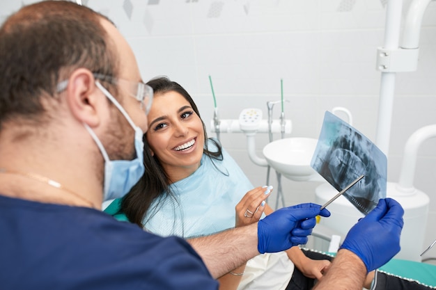 Les gens, la médecine, la stomatologie et le concept de soins de santé dentiste masculin heureux montrant le plan de travail à la patiente au bureau de la clinique dentaire.