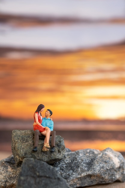 Gens miniatures Couple assis sur une plage de la mer avec fond de coucher de soleil