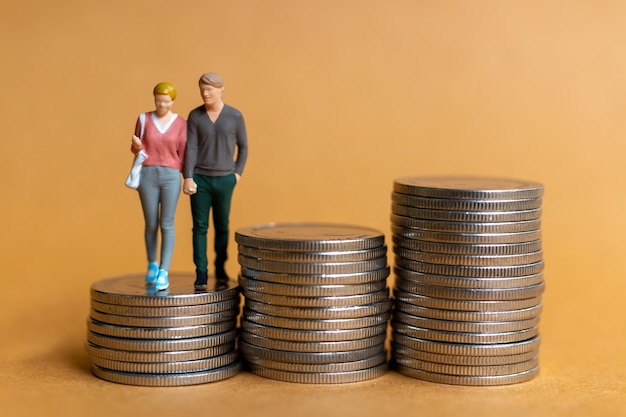 Photo gens miniatures couple heureux debout sur une pile de pièces