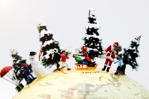 Gens miniatures: les enfants s'amusent avec le père Noël et le bonhomme de neige sur le globe.