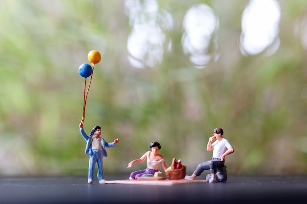 Gens miniatures: famille heureuse assis sur le tapis lors d'un pique-nique dans un parc