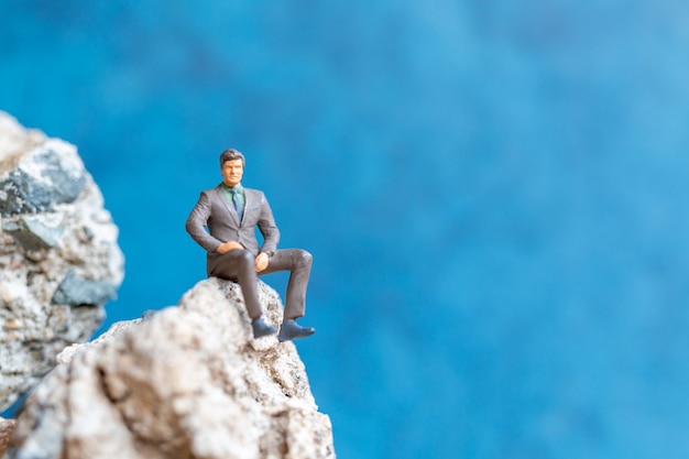 Gens miniatures Homme d'affaires assis sur le rocher avec fond bleu