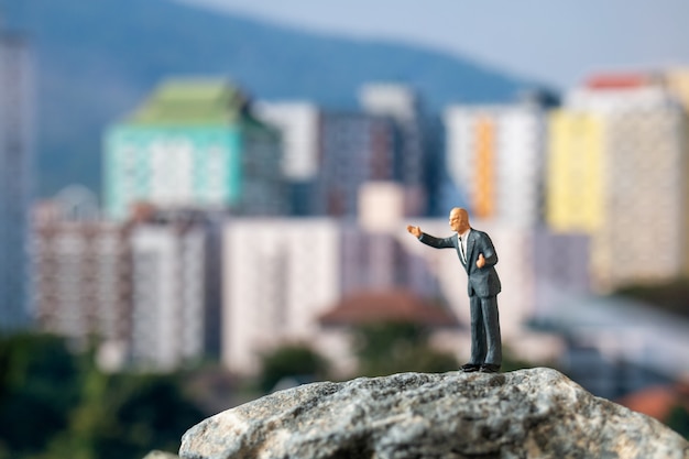 Gens miniatures, homme d'affaires debout sur le rocher avec bâtiment