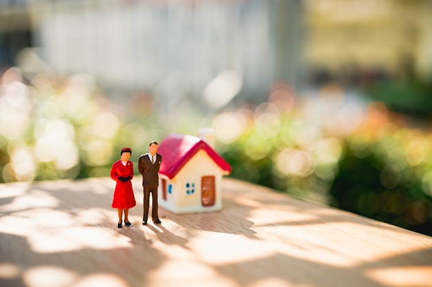 Gens miniatures, homme et femme debout avec mini maison sur fond de bokeh nature verte en utilisant comme r