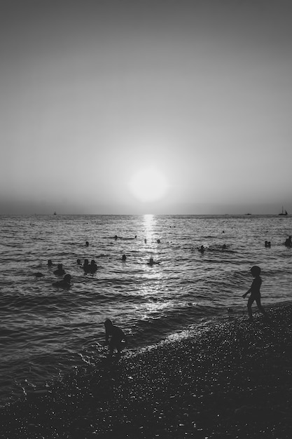 Les gens nagent dans la mer le soir au coucher du soleil, photo noir et blanc