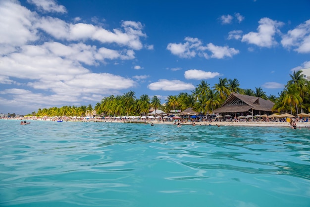 Les gens nagent près de la plage de sable blanc avec parasols bungalow bar et palmiers cocos turquoise mer des Caraïbes Isla Mujeres island Mer des Caraïbes Cancun Yucatan Mexique