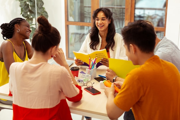 Des gens positifs. Des internationaux ravis assis à table tout en pratiquant une langue étrangère