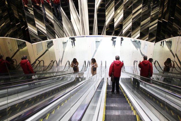 Les gens prennent des escaliers mécaniques avec des murs en miroir dans le centre commercial Les gens prennent des escaliers mécaniques avec des murs