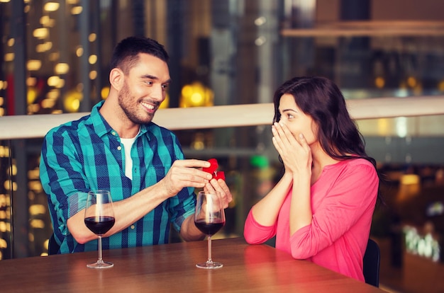 gens, proposition, amour, couple et concept de vacances - homme souriant donnant une bague de fiançailles en diamant à sa petite amie heureuse au restaurant