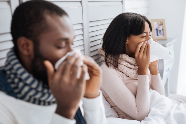 Les gens qui éternuent. Couple malade fatigué à la malheureuse tout en restant dans leur chambre et en éternuant