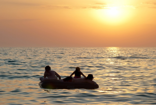 Les gens sur le radeau avec le coucher du soleil sur la mer