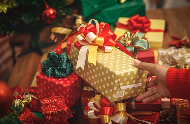 Les gens ramassent une boîte de cadeau de luxe avec un bel arc coloré de la table de fête d'un joyeux cadeau de Noël pour la célébration du festival d'hiver à la maison. Ajoutez du bruit pour s'adapter à l'image de style vintage