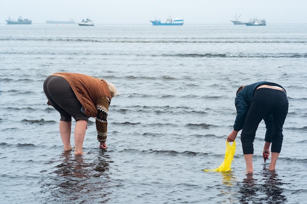 Les gens ramassent des coquillages sur le rivage à marée basse sur l'île de Kunashir sur fond de bateaux de pêche dans la mer